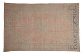 Distressed vintage Oushak carpet with faded rose pink field, central medallion, and pale blue floral motifs.