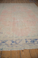 Distressed rose pink and ivory pile revealing wear on vintage Oushak rug, with cobalt border.