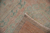 Distressed Oushak runner corner with worn pale pink and seafoam pile, hand-knotted reverse, and secured edge.