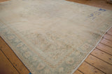 Corner of distressed Oushak rug with faded ivory, slate blue patterns, abrashed pile, and blue marks.