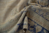 Folded distressed Oushak carpet pile showing worn ivory, cobalt blue, and muted green patterns.