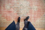 Distressed Oushak rug showcasing worn dusty rose, ivory medallion, and textured pile.