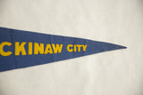 Vintage felt pennant detail with textured cobalt blue background and yellow 'CKINAW CITY' letters.