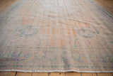 Distressed vintage Oushak rug showing worn pile, faded apricot, mint green, blue motifs, and fringe.
