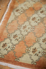 Angled view of a vintage Oushak rug's worn texture and pale rust floral trellis pattern.