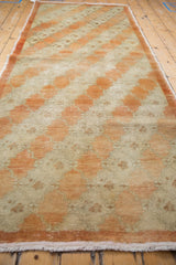Angled view down the length of a distressed Oushak runner with a diagonal trellis design in rust and ivory.