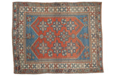 Distressed Melas carpet with rich brick red field, blue geometric medallions, and stepped borders.