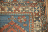 Distressed vintage Melas rug corner, featuring faded geometric patterns in blue, red, and ivory.