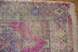 Distressed Oushak rug corner with stepped geometric floral border, aubergine, green, silver, and fringe.
