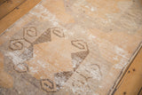 Distressed Oushak rug with worn gold, charcoal, and ivory ram's horn motifs.