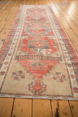Distressed Oushak runner's textured pile, with beige ground and charcoal and red pinwheel motif.