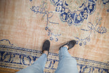 Distressed Oushak carpet texture with faded beige ground, cobalt blue vines, and border.