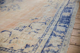 Distressed Oushak rug with faded beige field, foundation wear, and cobalt blue asymmetric border.