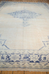 Textured vintage Oushak rug showing wear, faded cobalt blue border on ivory.