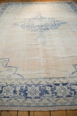 Textured vintage Oushak carpet's faded blue border and abrashed ivory field.