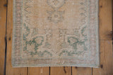 Distressed vintage Oushak rug close-up, worn pale seafoam green motifs on ivory field.