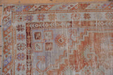 Stepped spandrel and barber pole border on a distressed Oushak rug corner in rust, ivory, lavender.