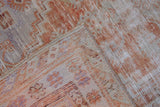 Folded distressed Oushak rug, revealing worn pile texture with faded rust, ivory, and blue patterns.