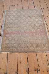 Distressed Oushak rug corner shows striking faded pink abrash, beige floral motifs, and visible wear.