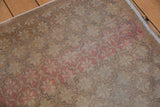 Distressed Oushak rug's worn texture showing pink floral buds and dye lot abrashes.