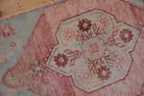 Distressed Oushak rug detail: abrashed raspberry field, ivory, sea foam floral motifs.