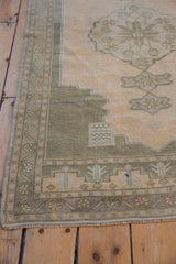 Distressed Oushak rug corner showing sage green spandrel and decorative border with worn pile.