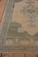 Distressed vintage Oushak rug corner showing soft beige pile, sage border, and natural fringe.