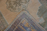 Hand-knotted Oushak rug corner showing distressed pile, beige field, and patterned border.