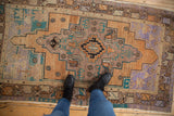 Faded vintage Oushak rug with geometric stepped medallion in terracotta, turquoise, and lavender.