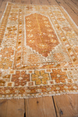 Distressed Oushak rug's lower corner, showing copper and gold pinwheel buds with visible wear.