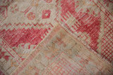 Folded corner of vintage distressed Oushak rug, showing worn cherry red pile and foundation.