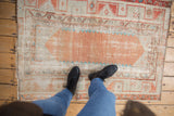 Person's feet on a vintage Oushak rug, highlighting distressed texture and patina.
