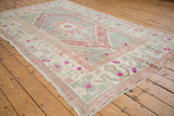 Lower corner of distressed Oushak rug featuring wide pink floral border and ivory field.