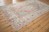 Distressed vintage Oushak rug corner showing decorative border motifs, ivory field, and magenta accents.