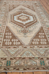 Vintage Oushak runner's distressed diamond finial, germinating plants, beige and brown hues.