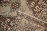 Distressed pile and fringe of a vintage Oushak rug, showing beige, brown, and dusty blue stepped patterns.