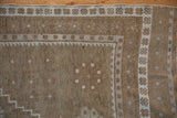 Distressed Oushak rug corner showing pale coffee brown field and ivory floral-geometric borders.