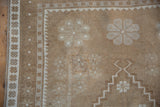 Pale coffee brown distressed Oushak rug with ivory serrated guls and pinwheel motifs.