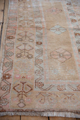Distressed beige Oushak rug with blush geometric border motifs and fringe detail.