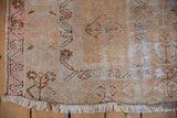 Distressed Oushak rug corner, showing soft fringes, worn beige, pink, and pale blue pile.