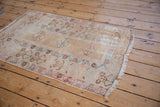 Distressed Oushak rug corner with fringe, showing time-softened beige and blush floral border.