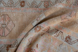 Distressed Oushak rug showing worn pile in folded detail with beige, pink, and copper hues.