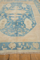 Distressed denim blue and ivory Oushak rug, featuring central cartouche, floral motifs, and fringe.