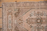 Distressed Oushak rug corner showing geometric stepped contour, worn pile, beige, brown, green.