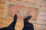 Distressed vintage Oushak rug with terracotta, sandalwood, and visible foundation underfoot.