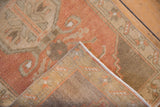 Folded vintage distressed Oushak rug corner showing terracotta pile, visible wear, and hand-knotted reverse.