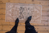Small distressed Oushak mat with faded beige, sand and charcoal tribal motifs.