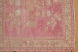 Distressed pink Oushak rug corner with abrash field and a pale beige geometric border.