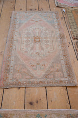 Distressed pink and beige Oushak rug bottom edge with aged patterns and fringe.