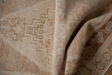 Distressed vintage Oushak rug's folded pile, showing even wear and faded ivory geometric pattern.